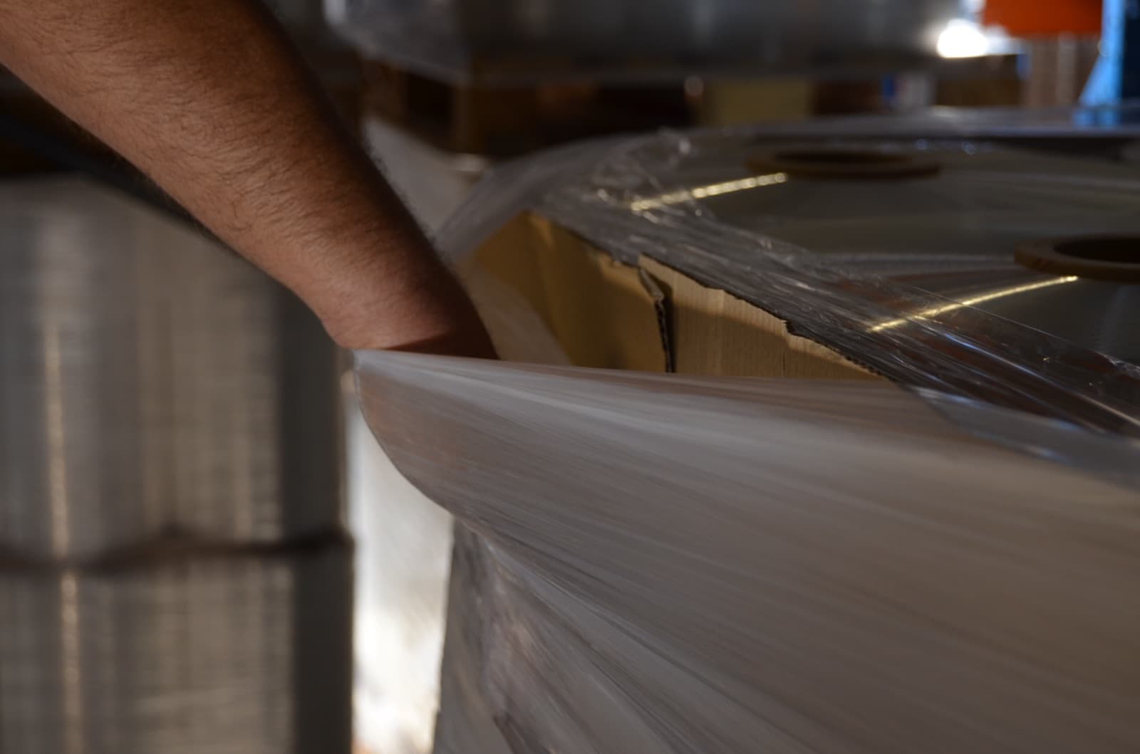 A hand pressing into the top corner of a pallet wrapped in reinforced film — the load does not give