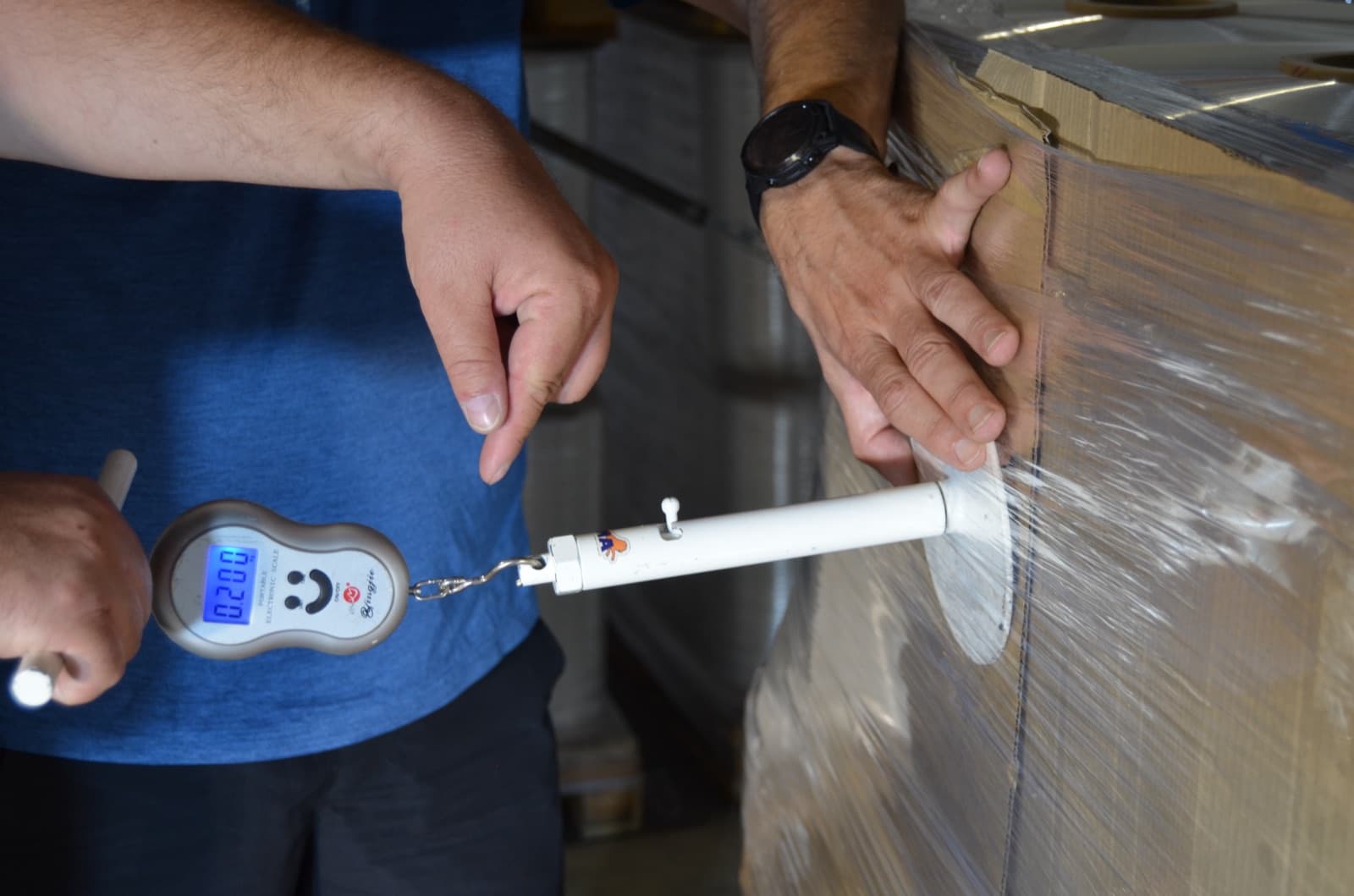 Load-stability testing at the Gilau plant: a digital force gauge measures how hard the wrap holds a pallet, in kilograms per square inch