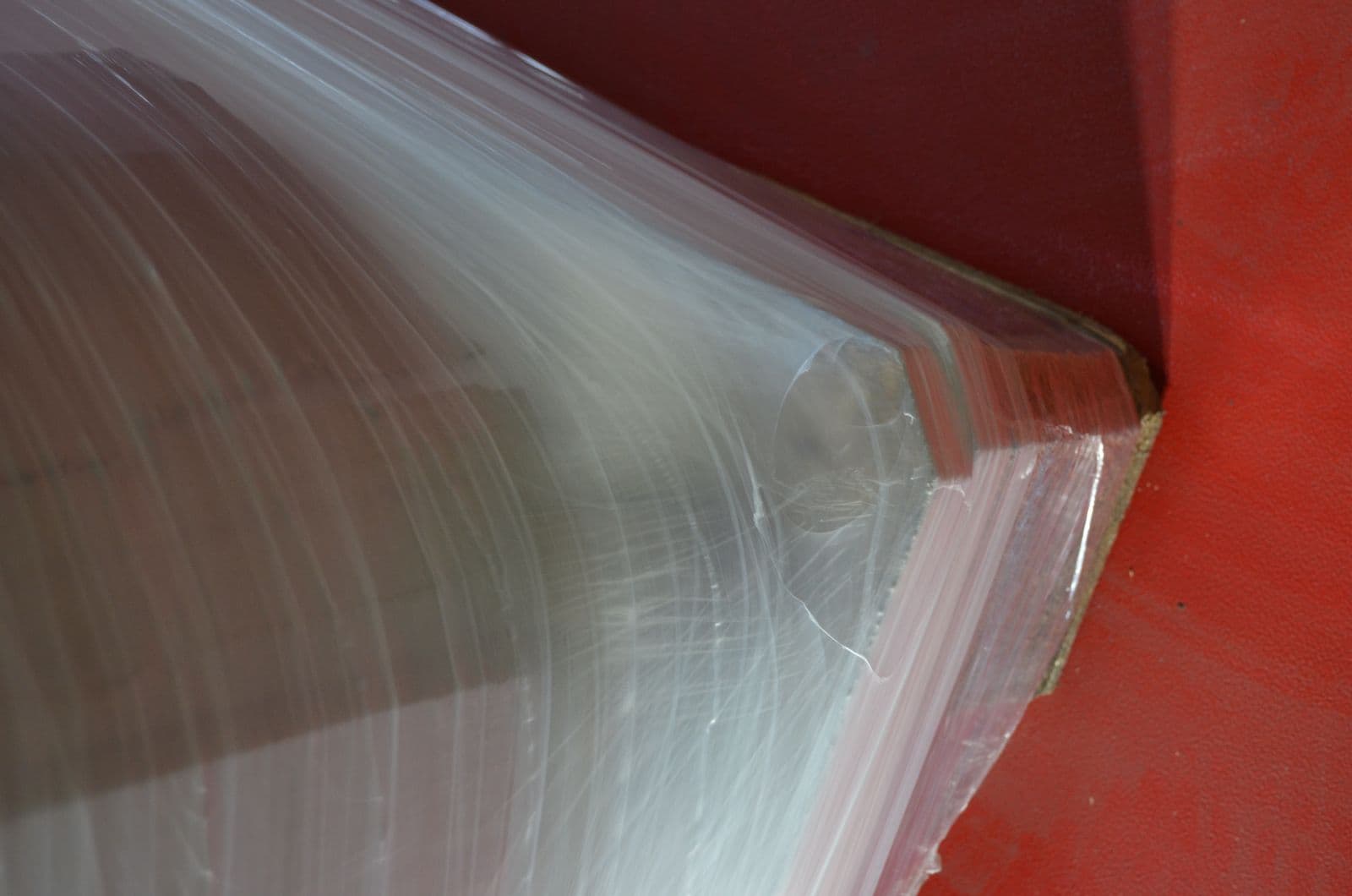 A Supersonic-wrapped pallet corner where the film has split — and the tear has stopped dead, held by the reinforcing lines instead of running on into the web